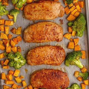 Overhead view of a full sheet pan with four pork chops, sweet potatoes, and broccoli.