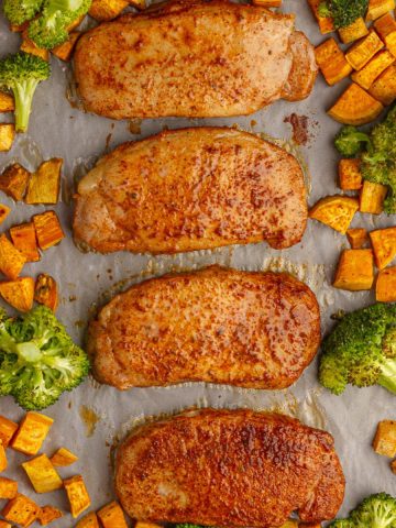 Overhead view of a full sheet pan with four pork chops, sweet potatoes, and broccoli.
