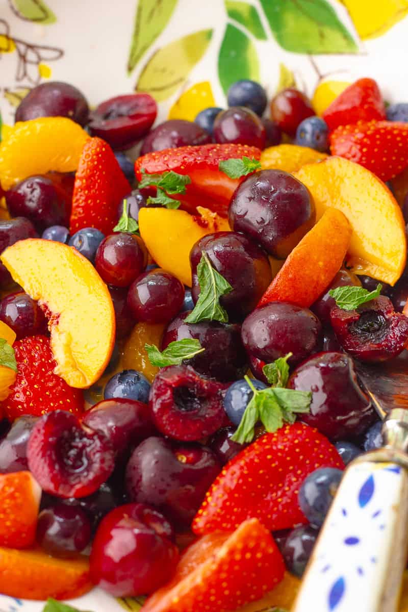A vibrant overhead view of summer fruit tossed with mint, ready to be served in a painted bowl.