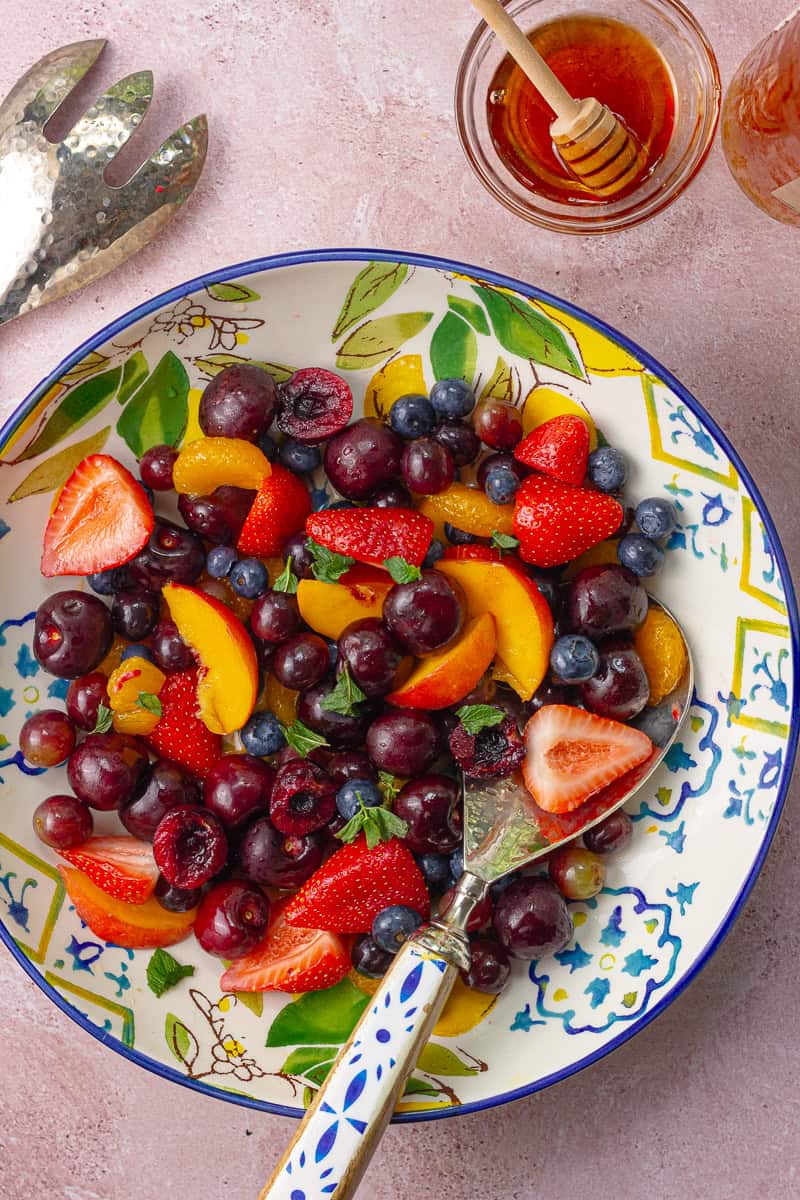 Sliced peaches, cherries, and berries glistening in the bowl, topped with fresh mint leaves.