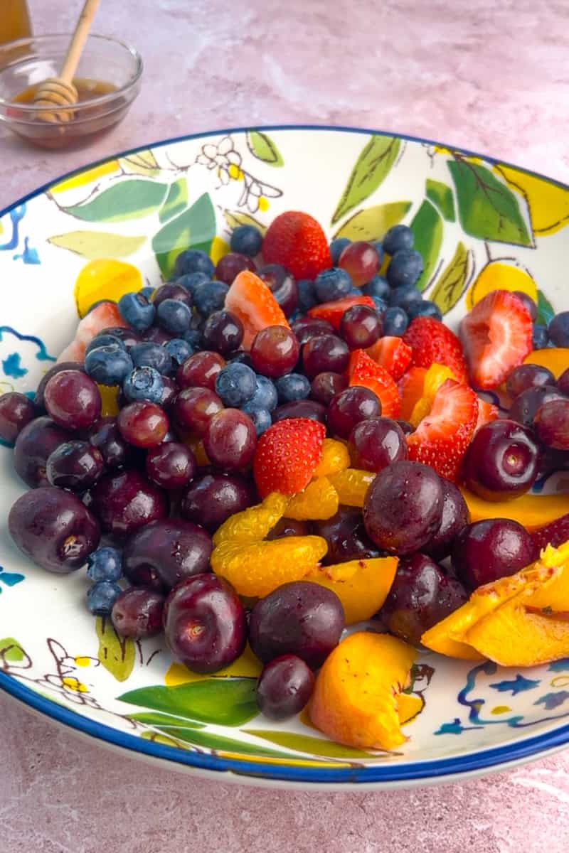 An overhead look at the full fruit salad with a honey jar and peach wine bottle beside the serving bowl.