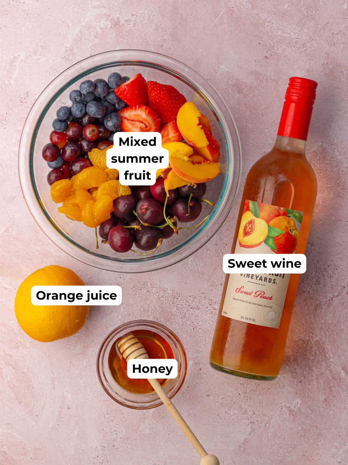 All the ingredients for sangria fruit salad laid out, including fresh fruit, peach wine, orange juice, and honey.