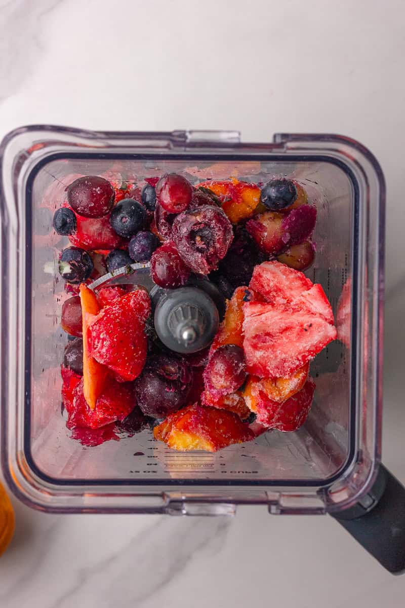 A top-down view of frozen mixed fruit inside a blender, ready to be blended.