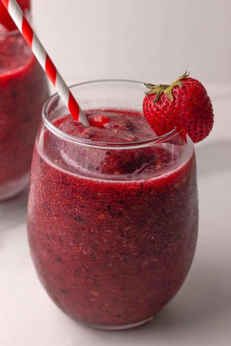 Two glasses of sangria slushie with fresh strawberries and striped straws on a white background.