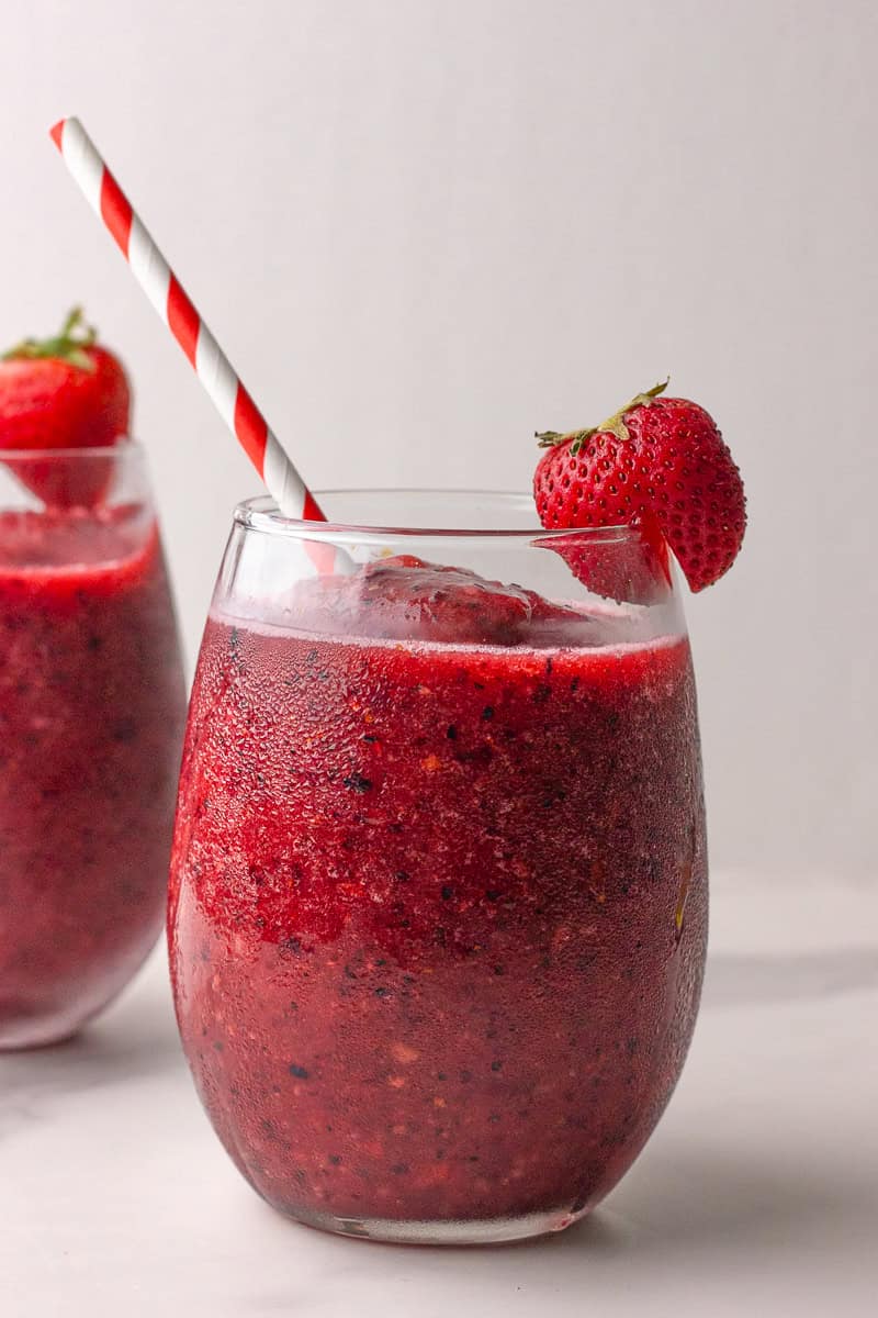 A close-up of a sangria slushie served in a glass with a red and white striped straw and fresh strawberry garnish.