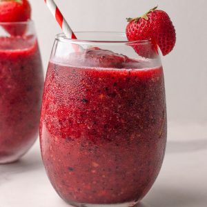 A close-up featured image of a sangria slushie in a glass with a strawberry and striped straw.