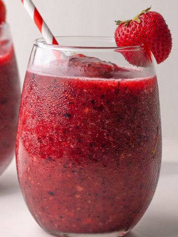 A close-up featured image of a sangria slushie in a glass with a strawberry and striped straw.