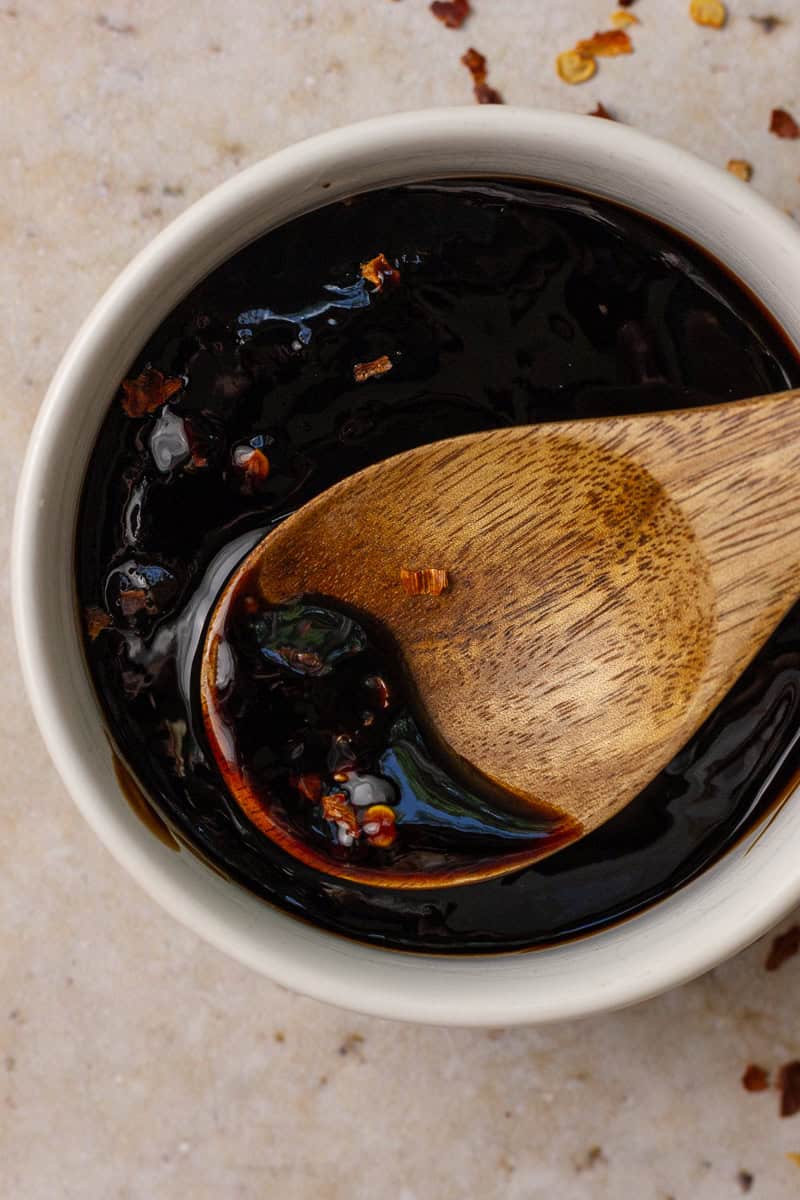 A wooden spoon dips into the finished spicy balsamic glaze, showing its rich, glossy texture.