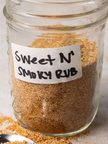 A close-up of a mason jar labeled “Sweet N’ Smoky Rub” with a spoonful of rub in the foreground.