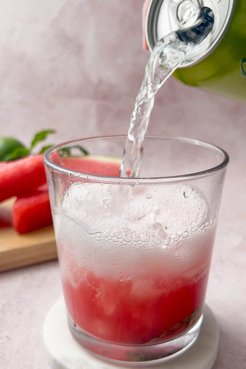 Sparkling water being poured into a glass of watermelon and mint for a fizzy virgin watermelon mojito.