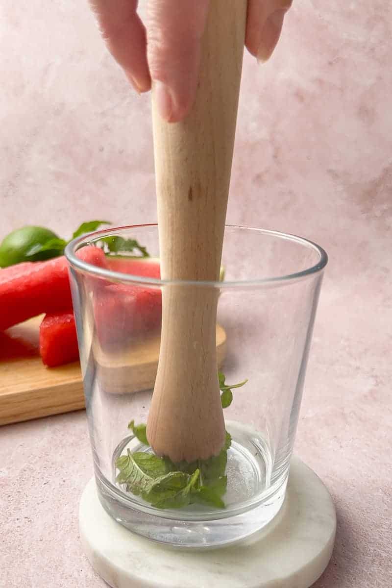 Fresh mint leaves being muddled in a glass to start a refreshing virgin watermelon mojito.