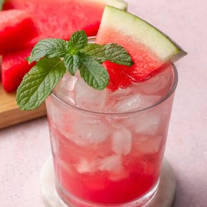 A refreshing glass of virgin watermelon mojito garnished with mint and a watermelon wedge, served on a marble coaster.