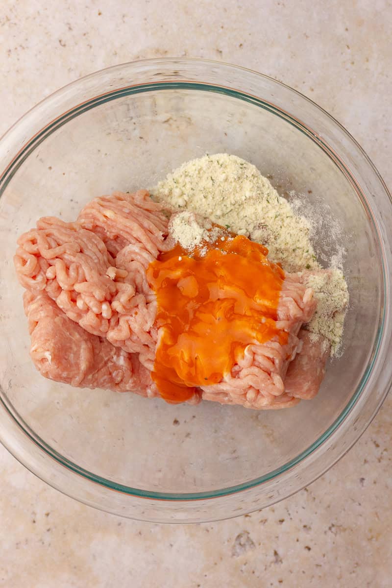 Ground chicken, ranch seasoning, and buffalo wing sauce sit in a glass bowl before mixing for buffalo chicken smash tacos.
