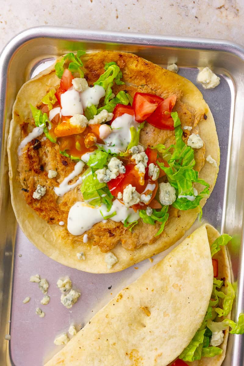 Assembled buffalo chicken smash taco is topped with lettuce, tomatoes, bleu cheese, ranch, and a drizzle of buffalo sauce.