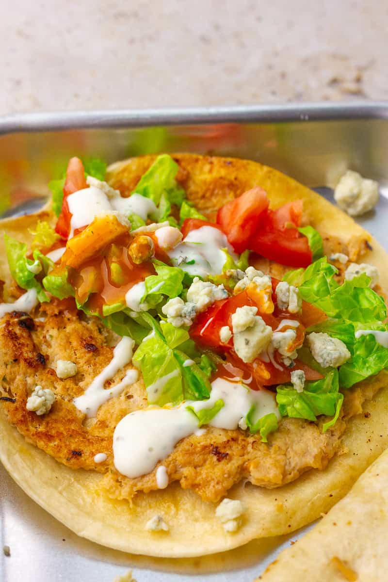 Close-up shows crispy chicken with fresh lettuce and tomato, bleu cheese crumbles, and ranch drizzle.