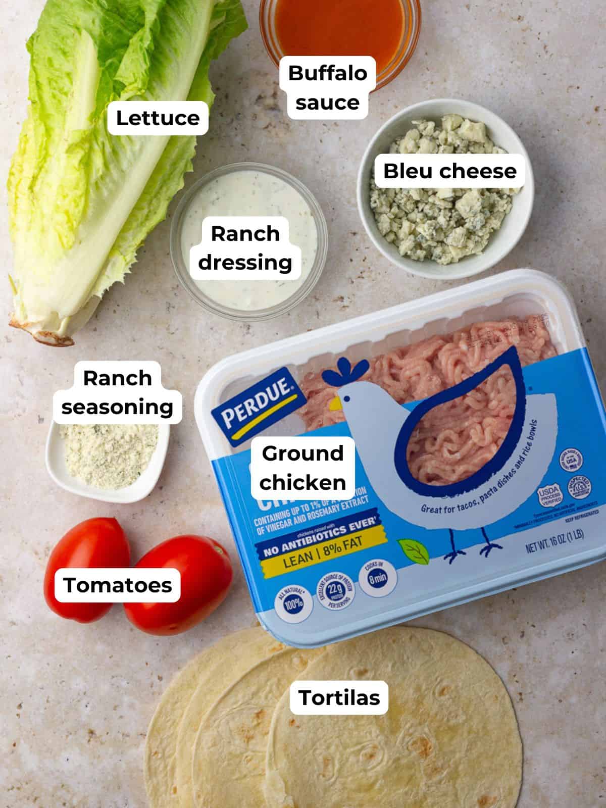 Flat lay shows ingredients for buffalo chicken smash tacos including ground chicken, tortillas, lettuce, tomatoes, ranch seasoning, ranch dressing, buffalo sauce, and bleu cheese.