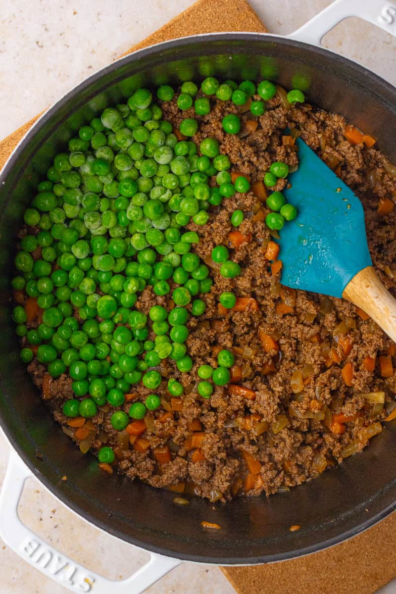 Frozen peas being added to the cooked beef and vegetable mixture in a Dutch oven.