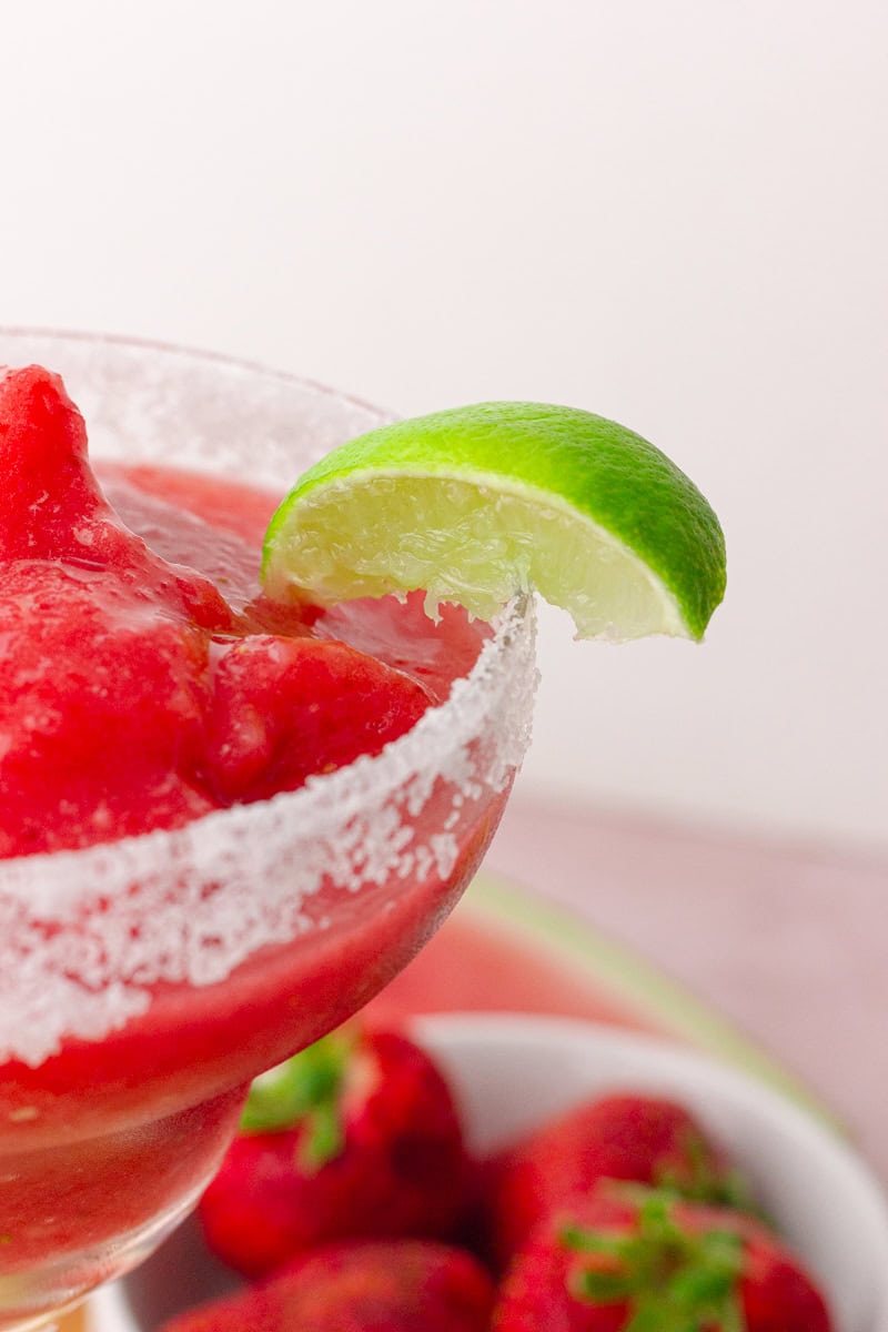 Close-up of a salt-rimmed margarita glass with a lime wedge and frozen margarita inside.