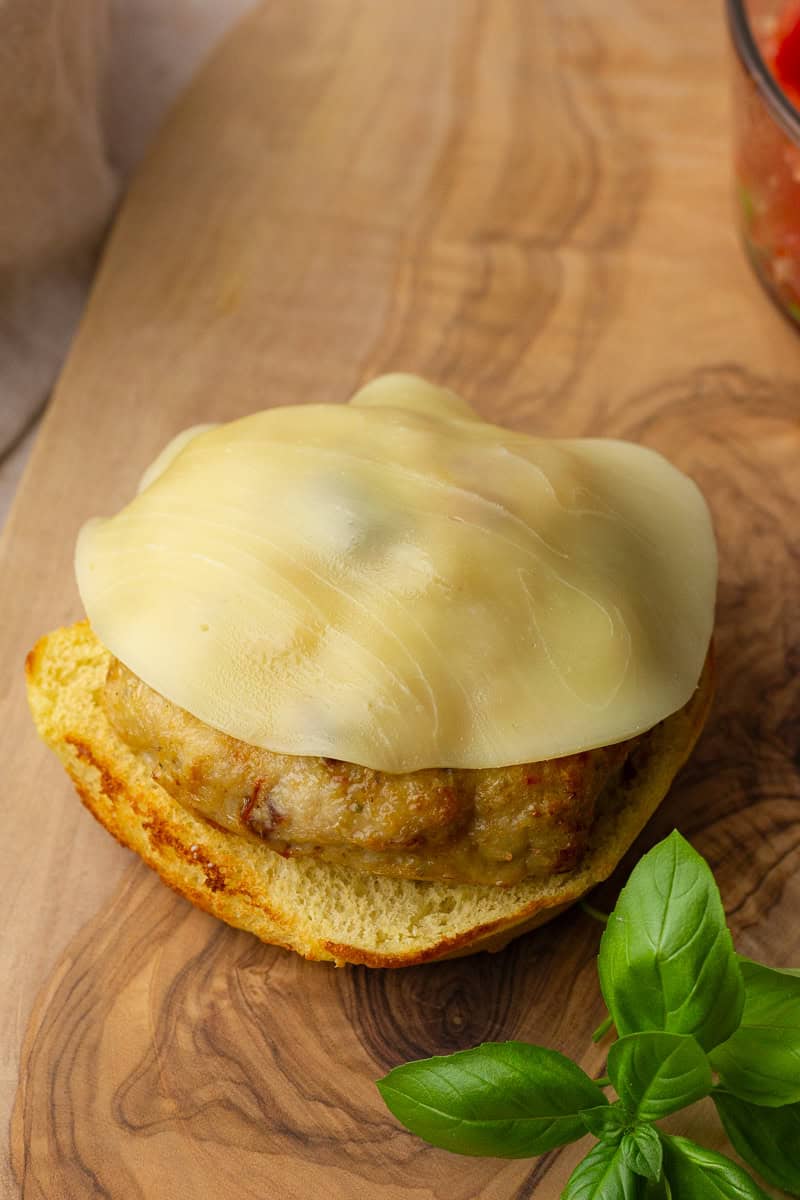Cooked chicken patty with slice of melted provolone cheese on toasted bun half.
