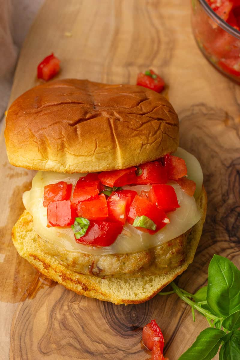 A close-up of a juicy bruschetta chicken burger topped with fresh tomato and basil mixture on a toasted bun.