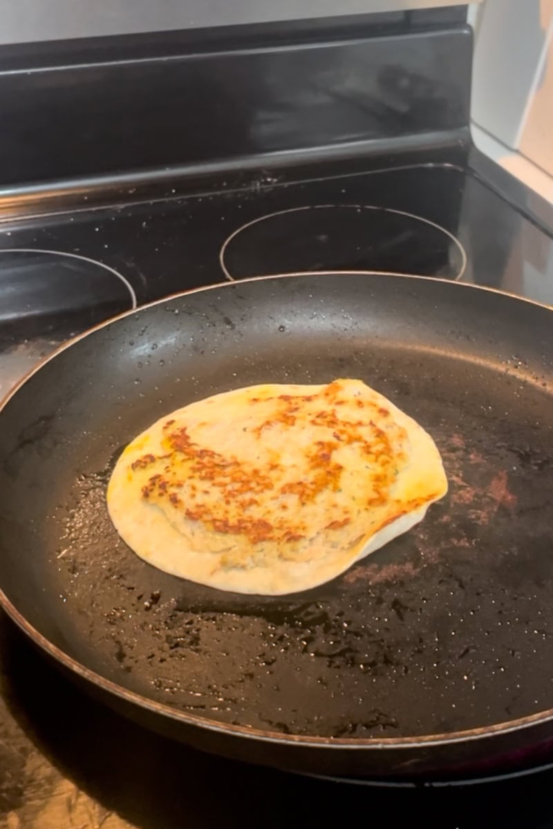 A tortilla cooks meat-side down in a skillet while the chicken layer browns.
