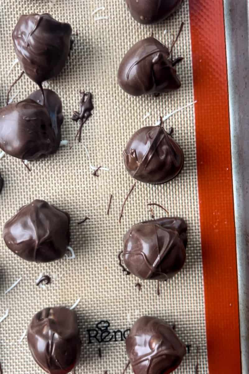 Dark chocolate-covered raspberries set on a silicone baking mat after being dipped.