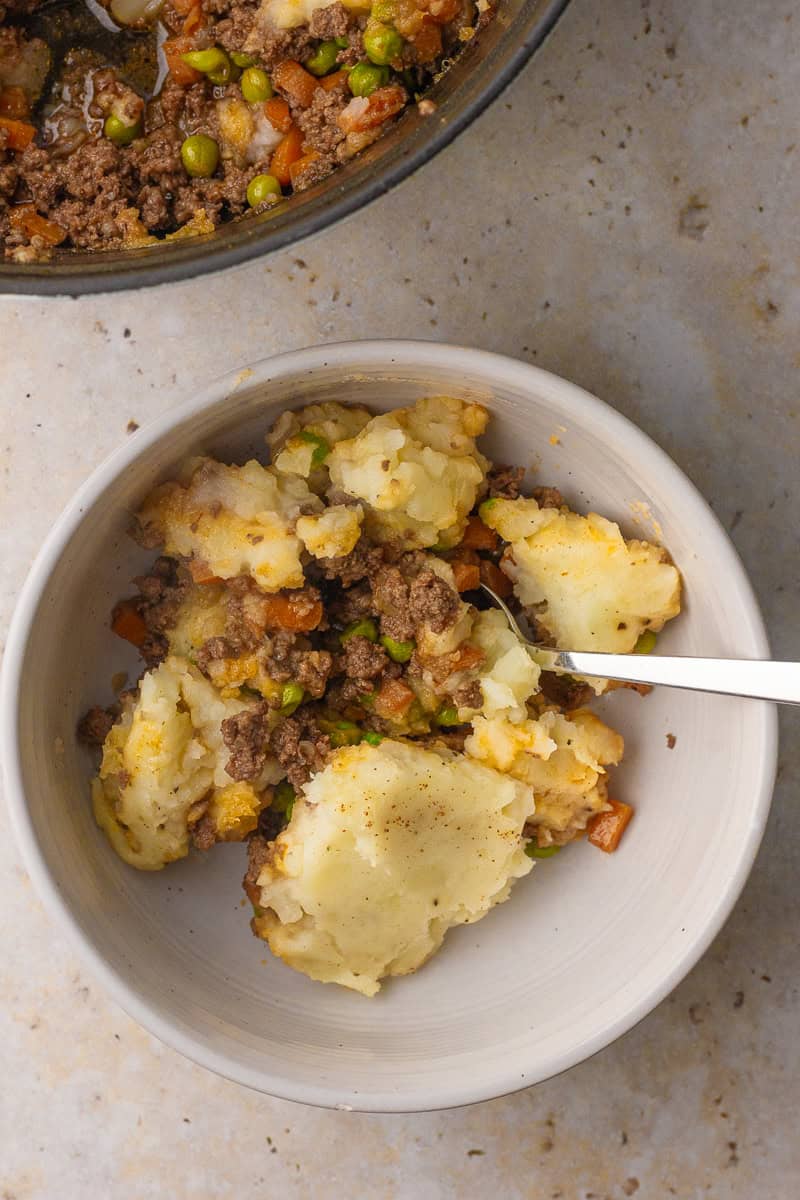 Bowl of Dutch oven Shepherd's pie with mashed potatoes, beef, peas, and carrots.