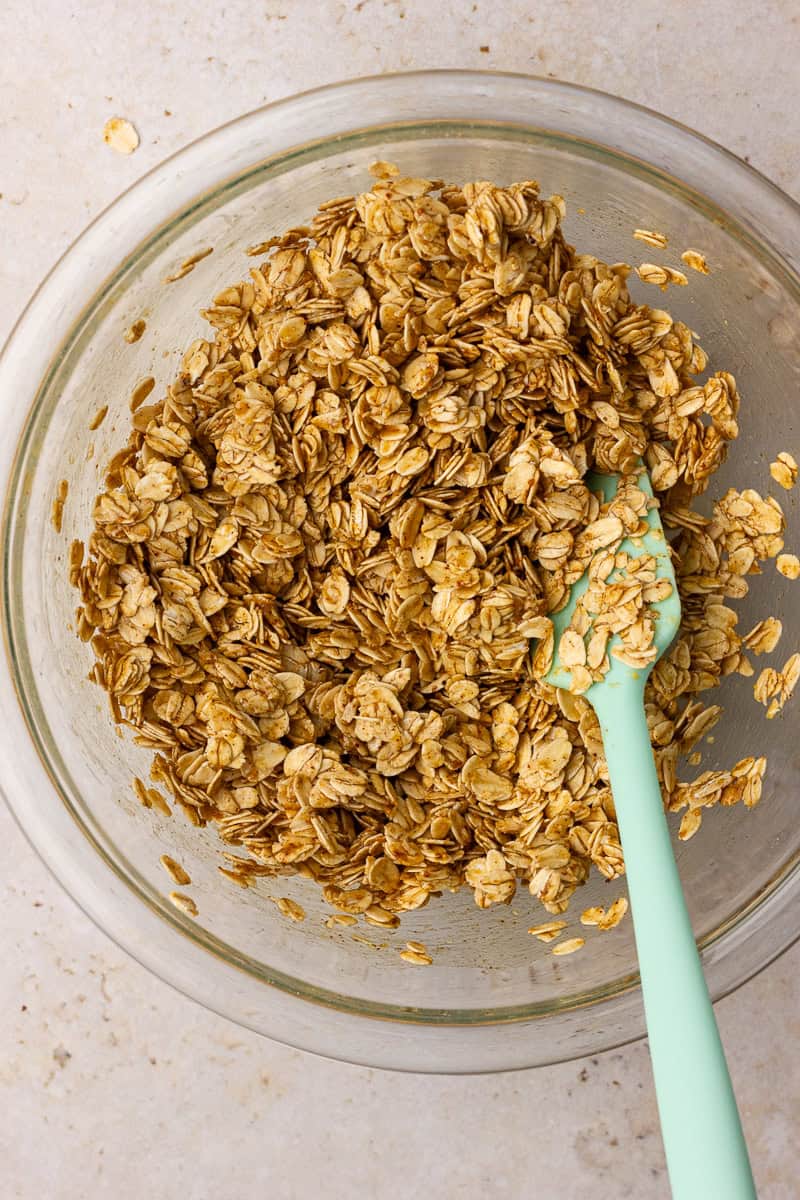 Rolled oats coated with honey, coconut oil, and almond butter in a glass bowl.