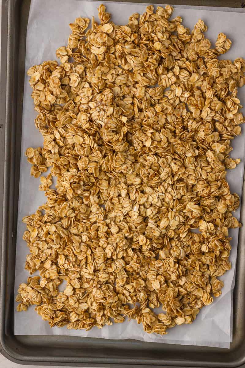 Pressed oat mixture spread in an even layer on a parchment-lined sheet pan before baking granola.