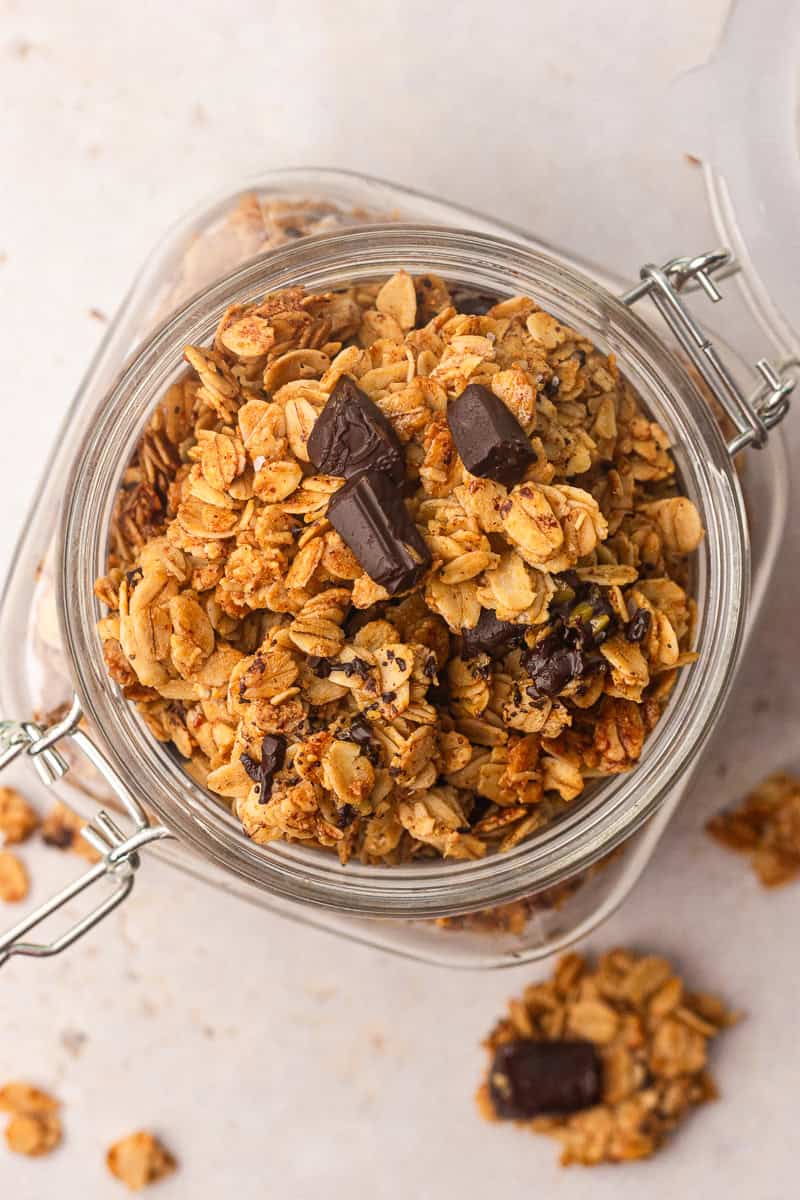 Overhead close-up of granola with dark chocolate pieces showing big toasted oat clusters.