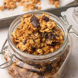 Hero shot of a glass jar filled with granola with dark chocolate chunks and crispy clusters.