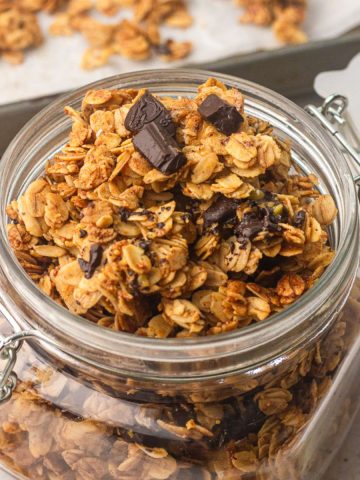 Hero shot of a glass jar filled with granola with dark chocolate chunks and crispy clusters.
