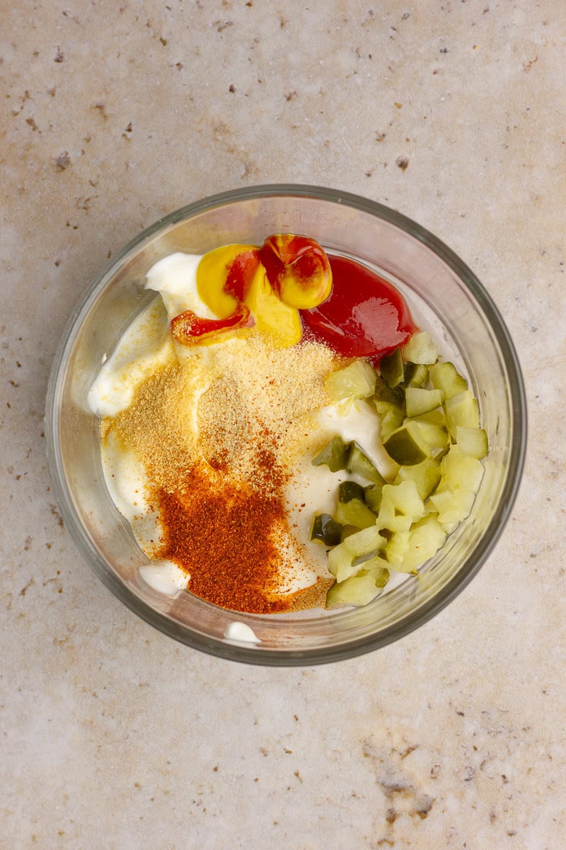 A glass bowl filled with light mayo, Greek yogurt, ketchup, mustard, chopped pickles, garlic powder, and paprika before mixing to make healthy Big Mac sauce.