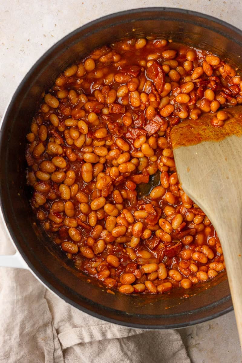 Baked beans simmering in a dutch oven until the sauce is thick. 