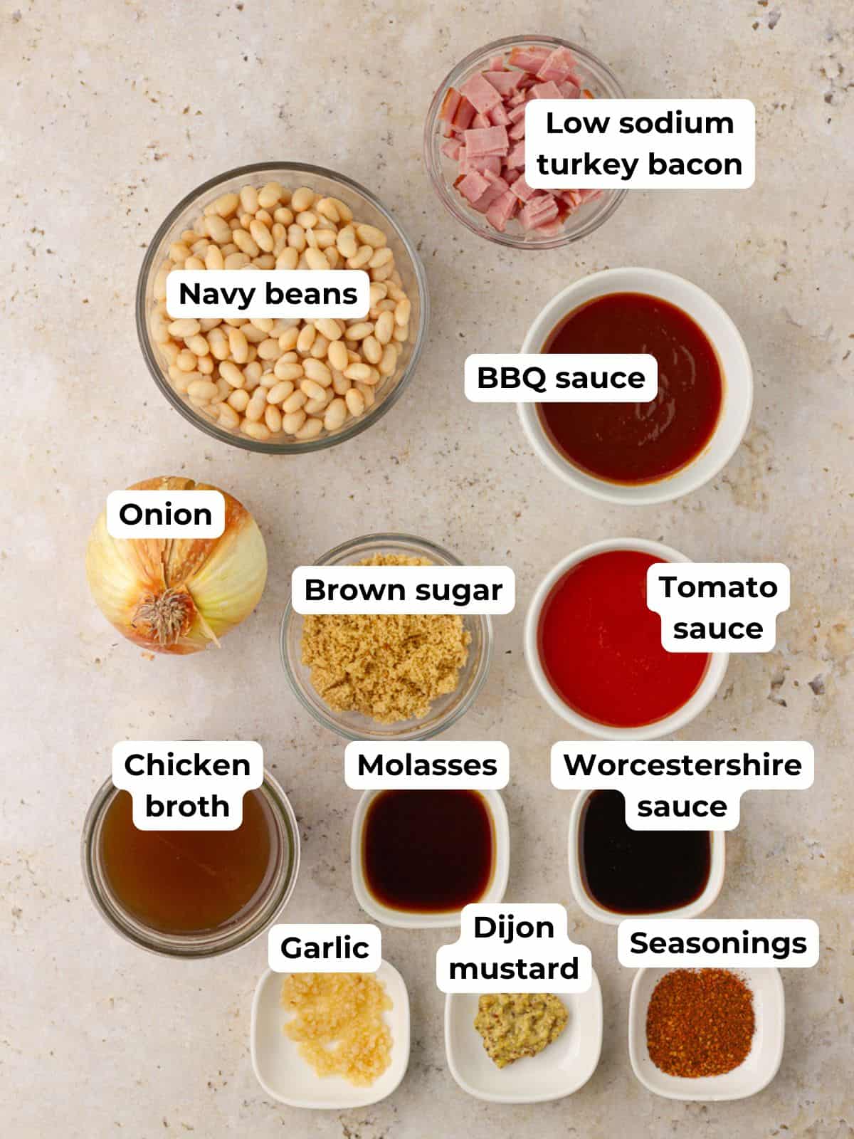 Flat lay of ingredients for low sodium baked beans including navy beans, turkey bacon, tomato sauce, BBQ sauce, broth, and spices.