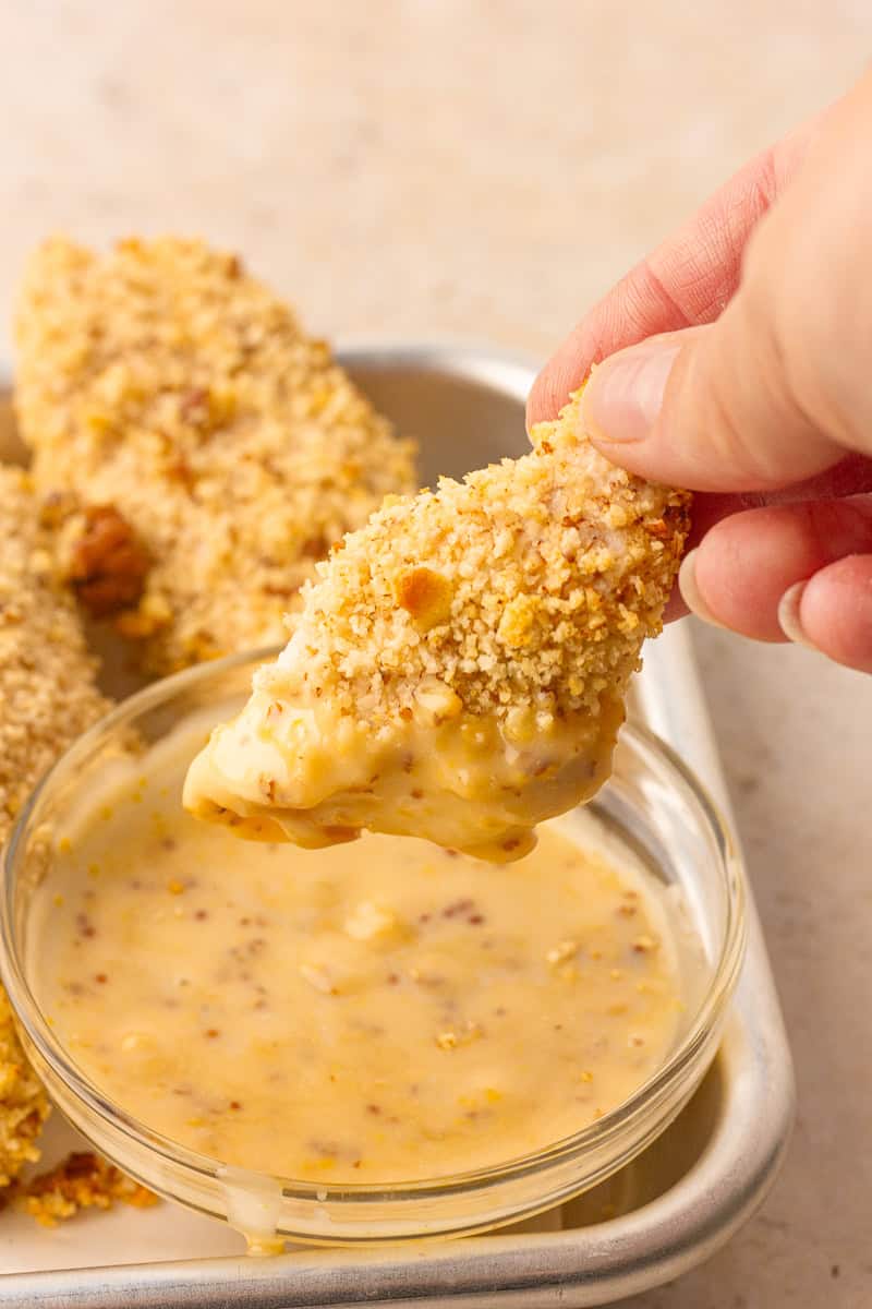 Air fryer pecan crusted chicken tender being dipped into creamy honey mustard sauce.