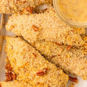 Overhead hero shot of pecan crusted chicken tenders with chopped pecans and honey mustard sauce.