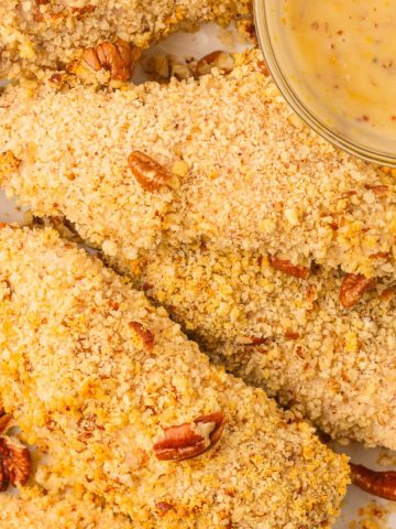 Overhead hero shot of pecan crusted chicken tenders with chopped pecans and honey mustard sauce.