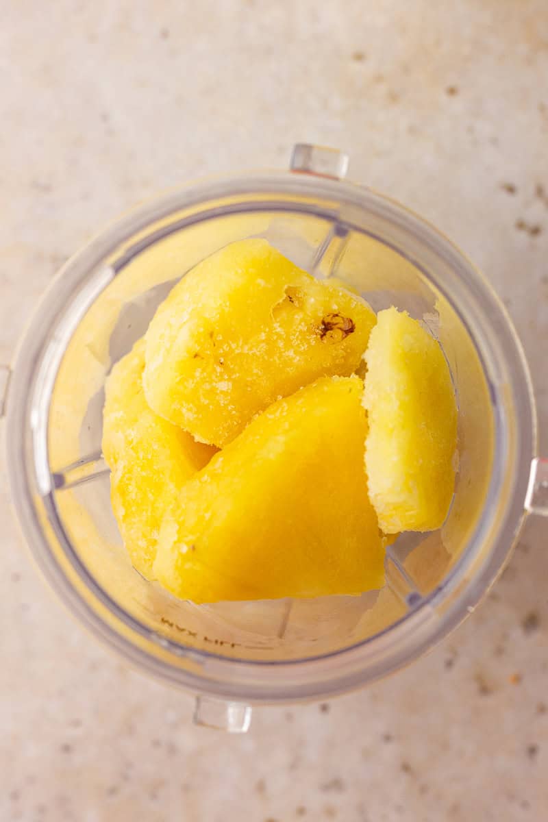 Frozen pineapple chunks in a blender cup ready to be blended.