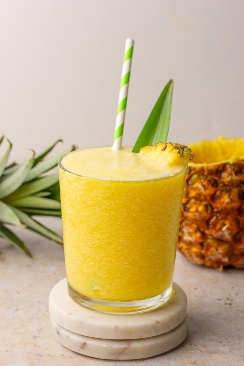 Pineapple slushie in a glass with a green-striped straw and pineapple garnish.