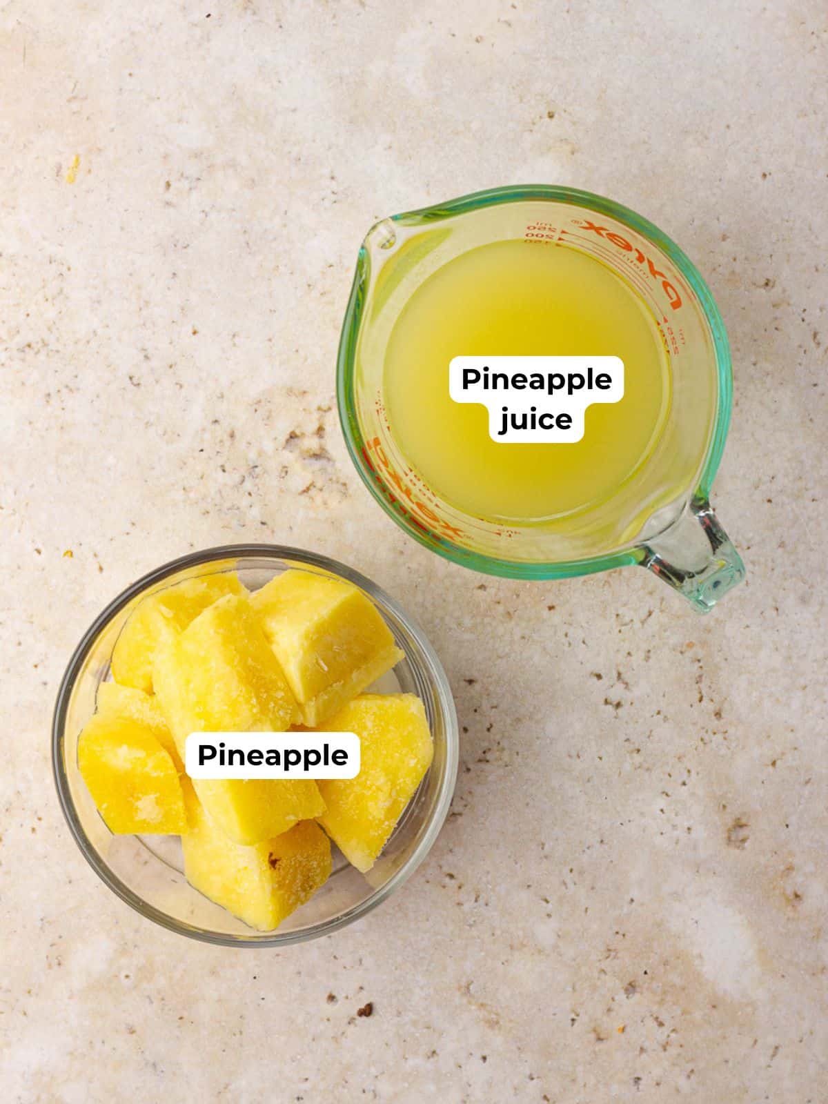  Frozen pineapple chunks in a bowl and pineapple juice in a measuring cup on a countertop.