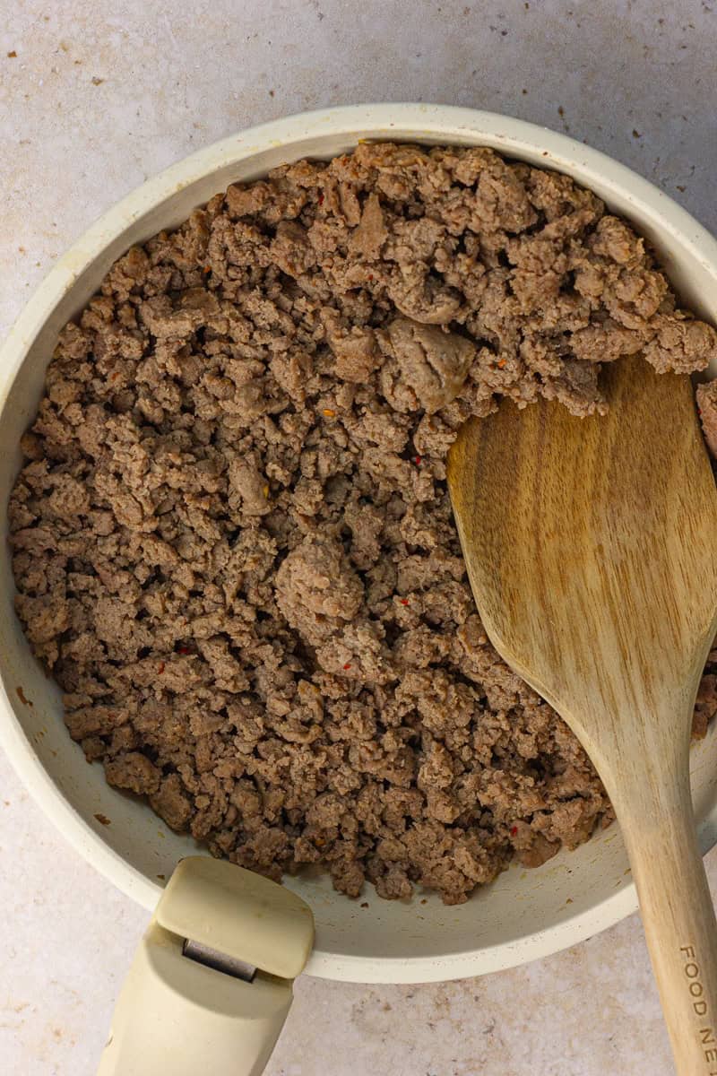 Browned turkey sausage crumbles in a skillet with a wooden spoon for pancake sausage muffins.