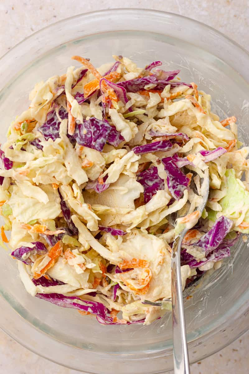 Creamy tri-color coleslaw in a glass mixing bowl with a spoon.