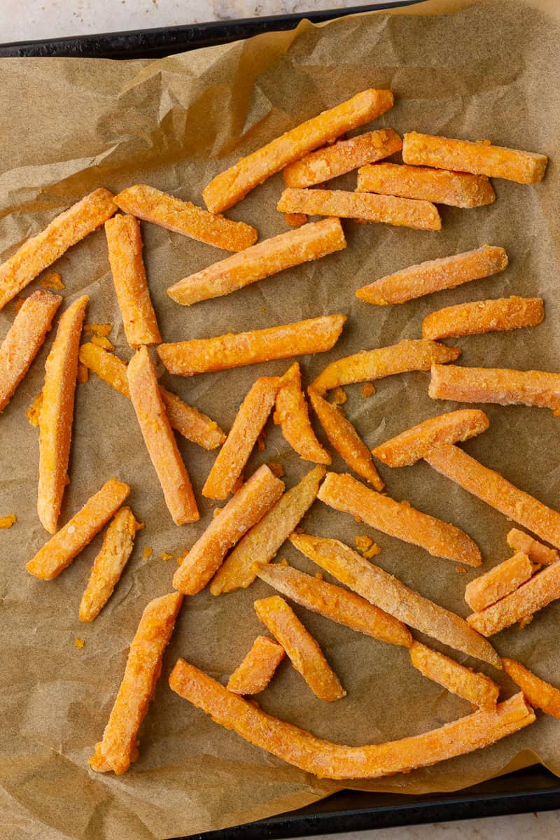 Frozen sweet potato fries spread on a parchment-lined sheet pan, ready for the oven.