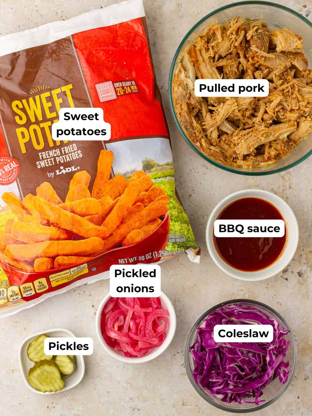 Flat lay of ingredients for a pulled pork bowl including fries, pork, BBQ sauce, slaw, pickles, and pickled onions.