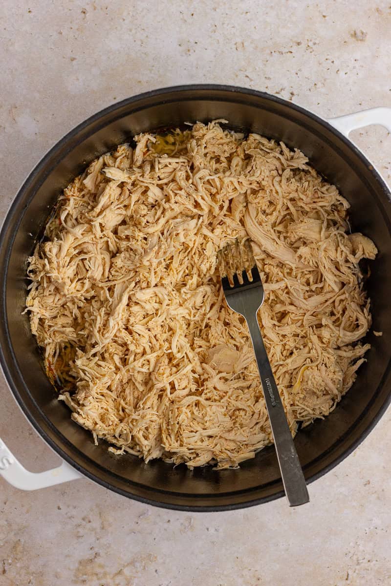 Shredded chicken in a white Dutch oven with a fork resting on top.