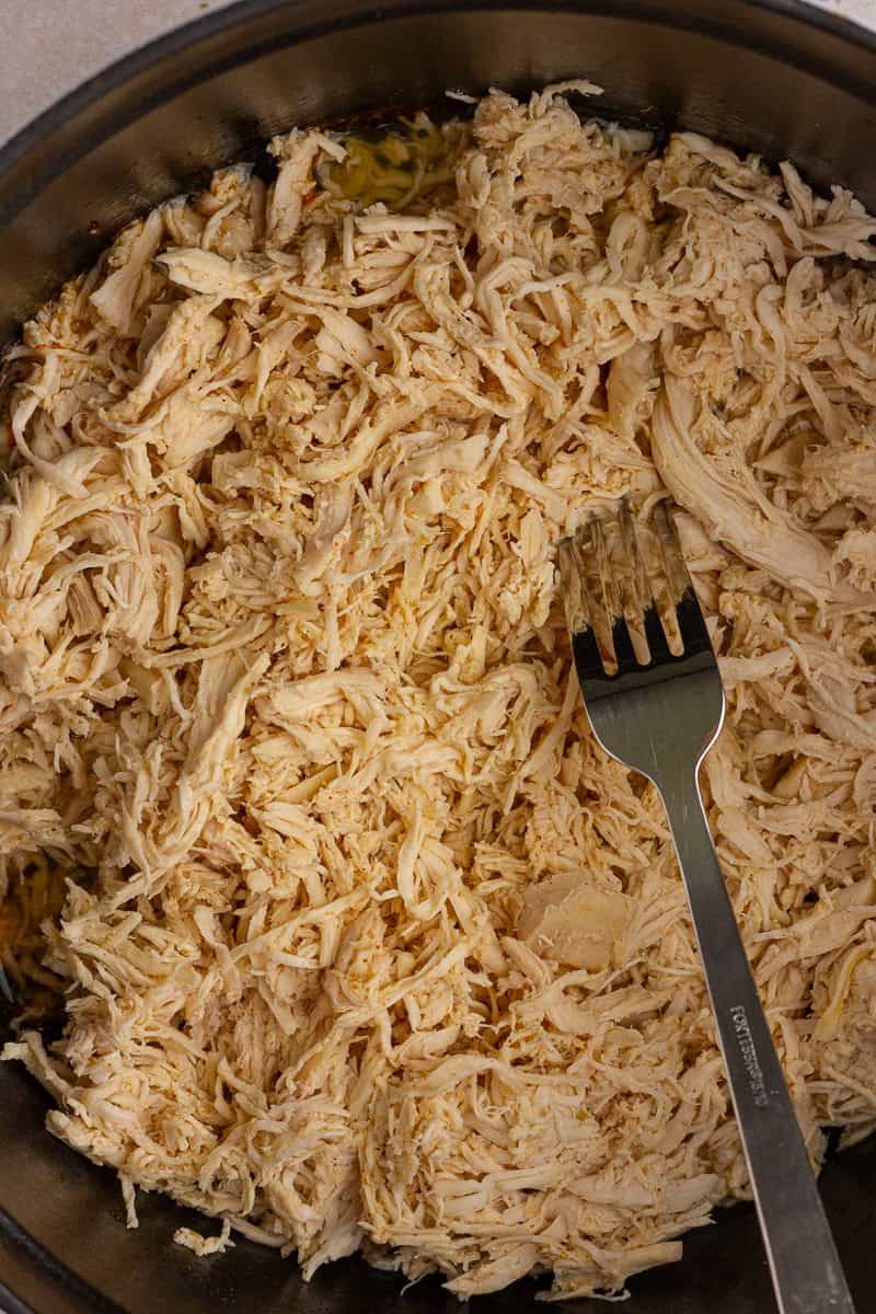 Freshly cooked shredded chicken inside a Dutch oven, with a fork resting on top.