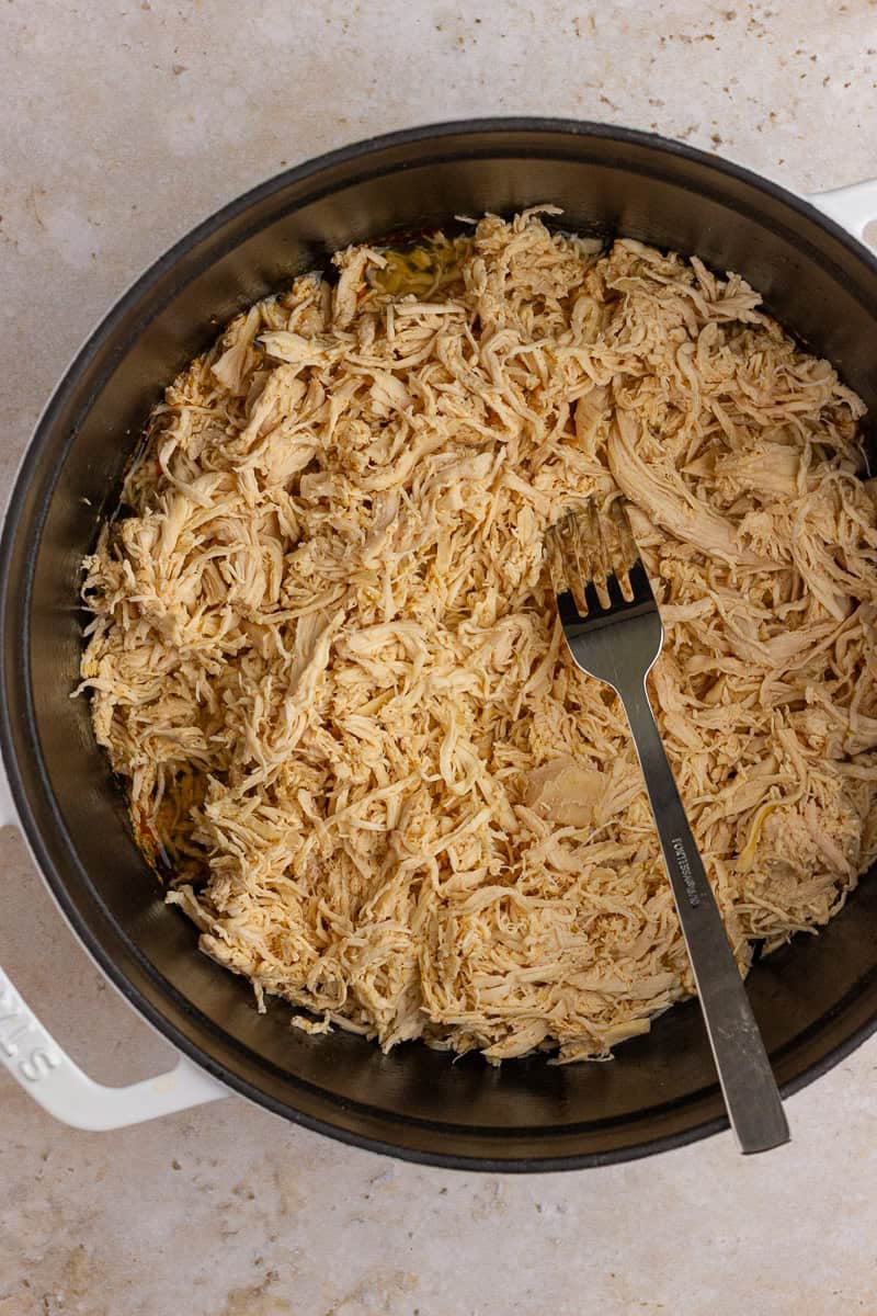 Close-up of shredded chicken in a Dutch oven with a fork.