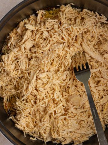 Shredded chicken filling a Dutch oven with a fork resting inside.