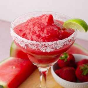 Salt-rimmed margarita glass filled with frozen strawberry watermelon margarita and garnished with a lime wedge.